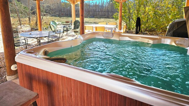 Un jacuzzi bajo una pérgola de madera con vistas a un patio trasero y mobiliario de exterior.