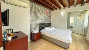 A hotel room with a bed, a wooden nightstand, a TV, a brick wall, and a ceiling with exposed beams. - İznik Otel (Iznik)