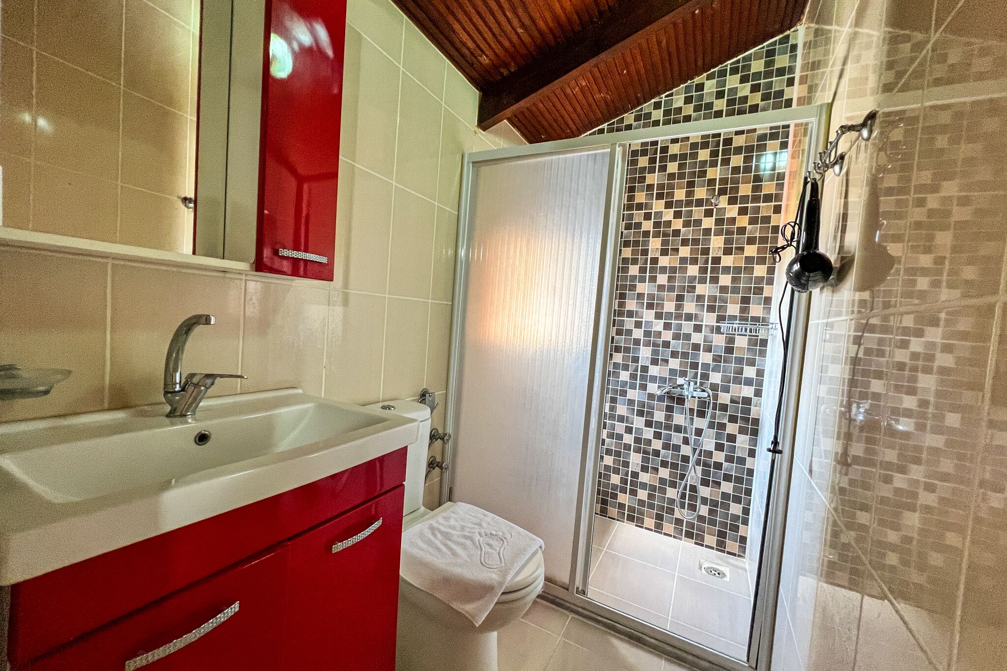 A bathroom with a white sink, red cabinet, and a shower with mosaic tiles.