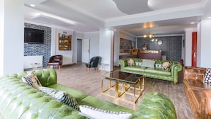A spacious living room with a green sofa, a leather couch, and a reception area with a brick wall and a clock. - İznik Otel (Iznik)