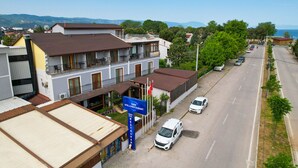 A hotel with a sign indicating it is a restaurant, a white van parked in front, and a street with cars and greenery. - İznik Otel (Iznik)