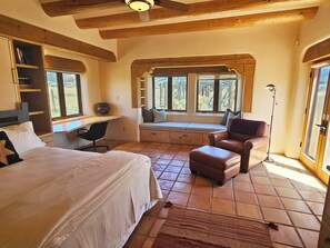 A bedroom with a large bed, a desk, a chair, and a window seat with cushions. - Sweeping panoramic mountain views, expansive adobe privacy wall system (Arroyo Seco)