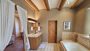 A bathroom with a wooden vanity, a large bathtub, and a shower area. - Sweeping panoramic mountain views, expansive adobe privacy wall system (Arroyo Seco)