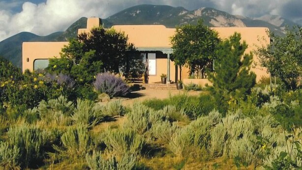 A modern house with a flat roof, surrounded by a garden with various plants and a mountain in the background. - Sweeping panoramic mountain views, expansive adobe privacy wall system (Arroyo Seco)