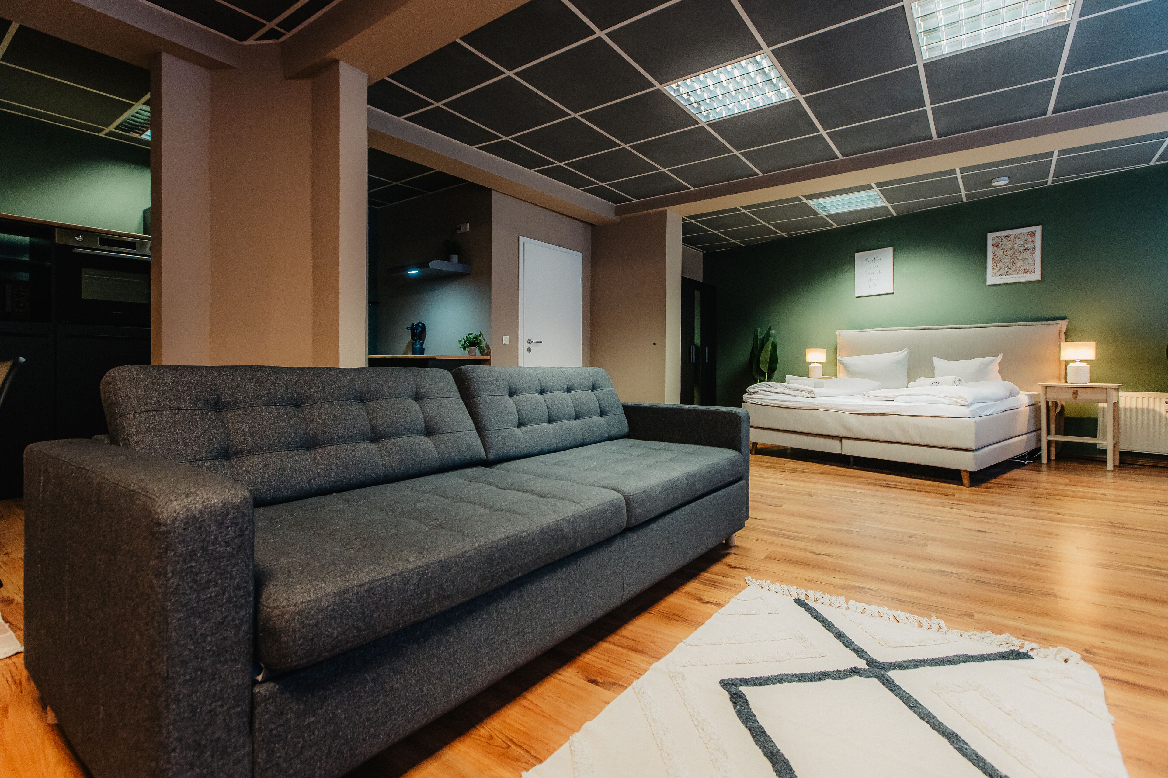 A modern bedroom with a grey sofa, a bed with white linens, and a wooden floor.