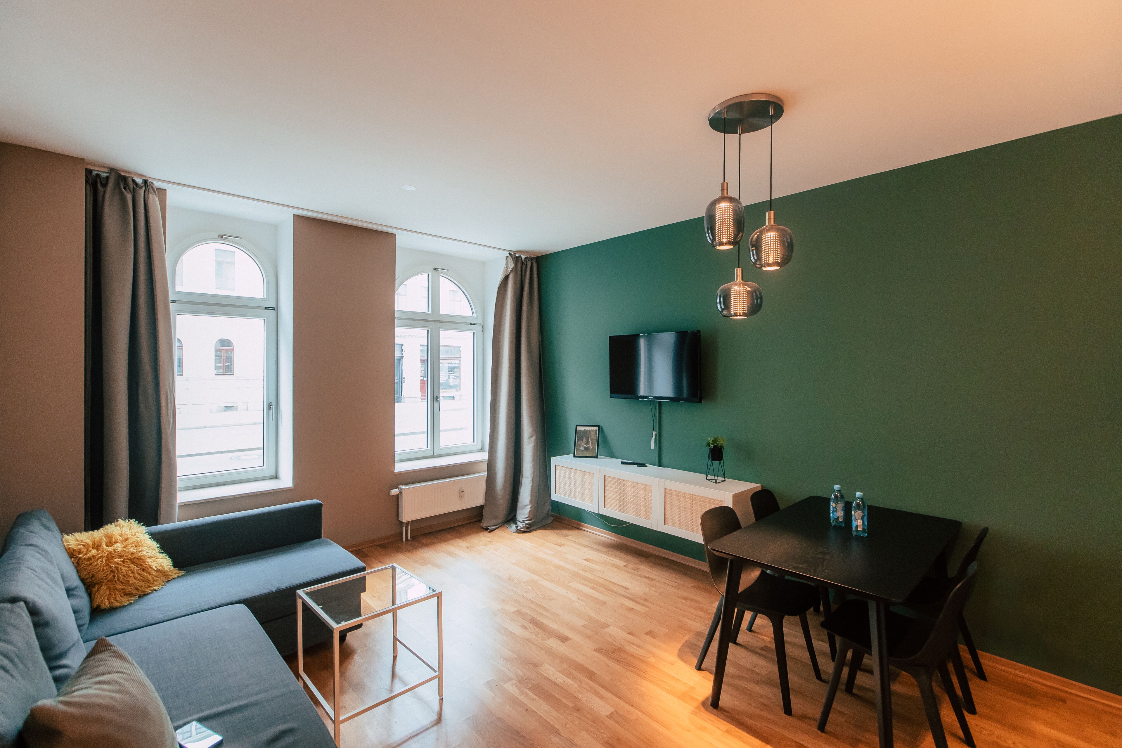 Una sala de estar moderna con un sofá, una mesa de comedor y un televisor montado en la pared.