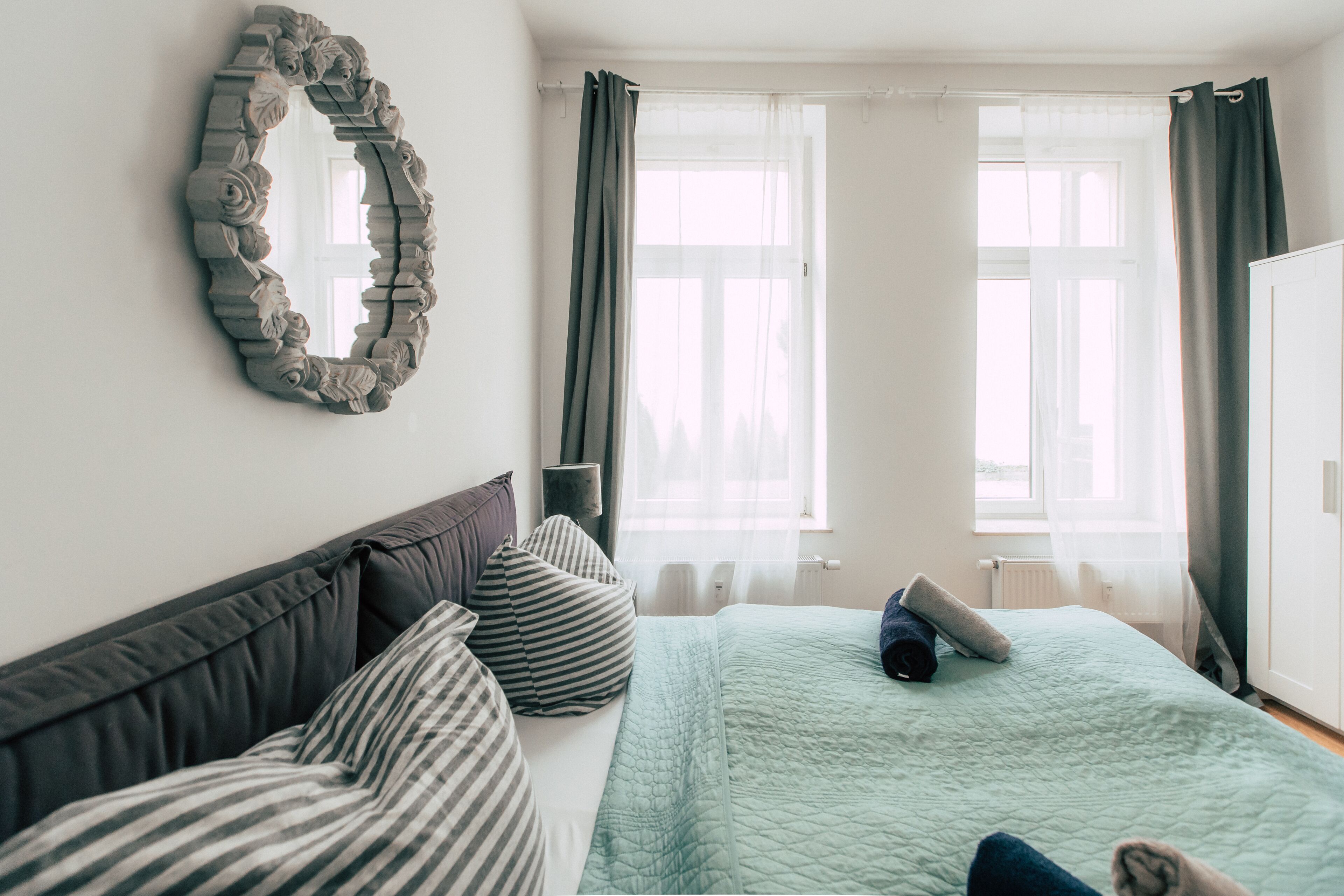 Una camera da letto con un letto, cuscini, uno specchio e una finestra con tende.