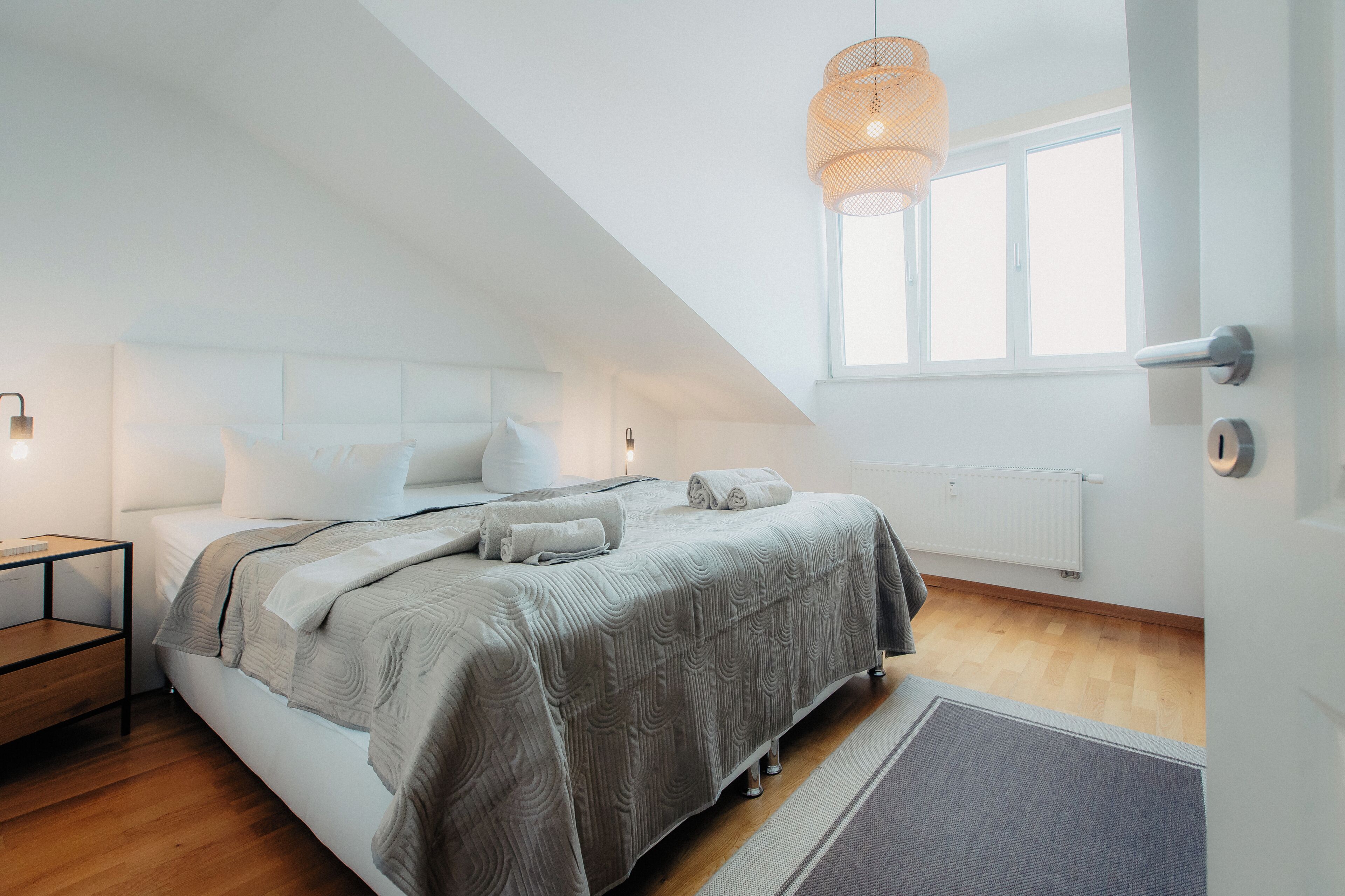 A bedroom with a bed, a nightstand, a window, and a hanging light fixture.