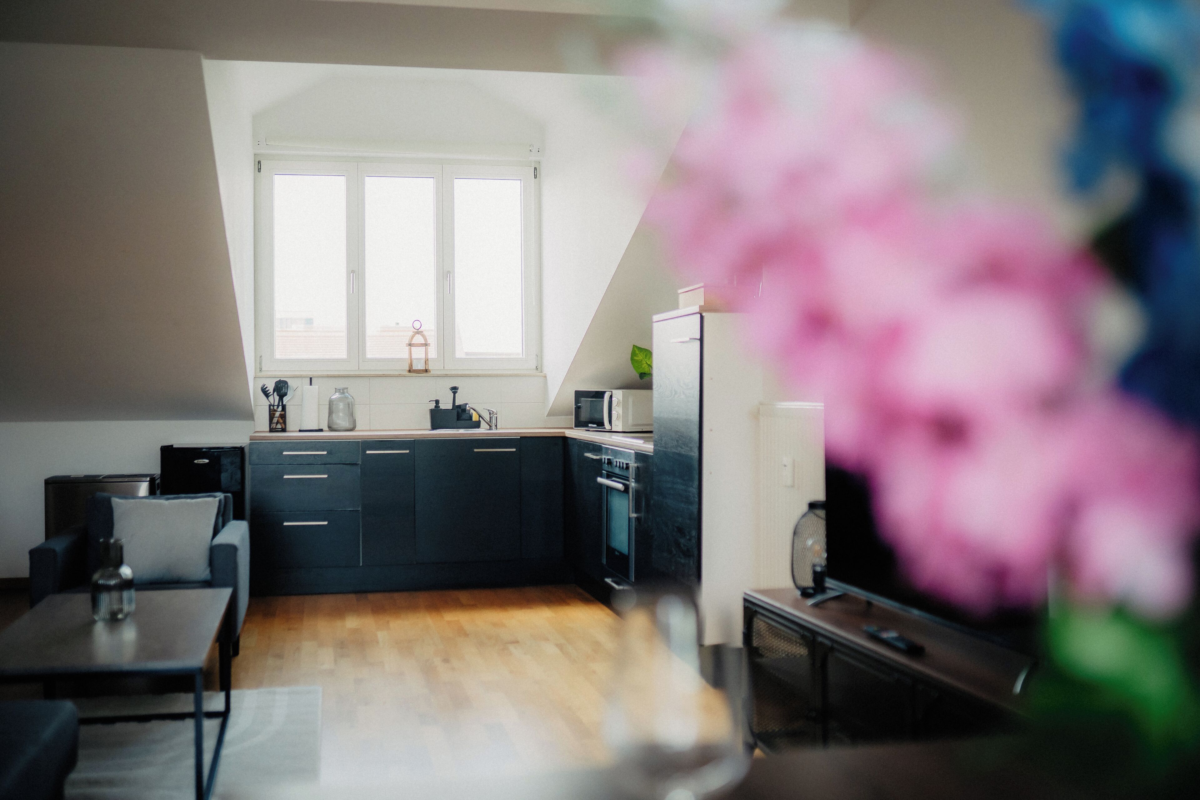 A modern kitchen with dark cabinetry, a window above the sink, and a dining area with a table and chairs.