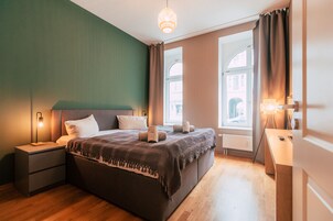 Un dormitorio moderno con una cama grande, lámparas de noche y vistas de la ciudad a través de amplias ventanas.