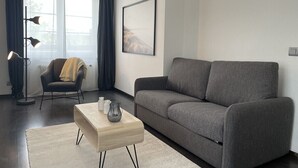 A modern living room with a grey sofa, a wooden coffee table, a floor lamp, and a chair with a blanket.