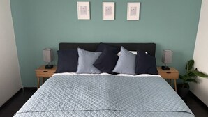 A neatly made bed with a quilted cover, two bedside tables with lamps, and a framed picture on the wall.