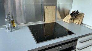 A kitchen with a stainless steel backsplash, a black induction cooktop, and a wooden cutting board.