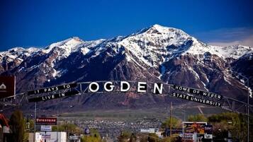 A mountain range with a sign reading "OGDEN HOME OF WEBER STATE UNIVERSITY" and a road leading into a town.