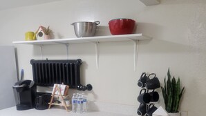 A kitchen with white cabinets, a countertop, a radiator, a coffee machine, a water dispenser, and a trash bin. - Beautiful Newly Renovated Basement Apartment (Ogden)