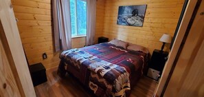 Quarto com painéis de madeira, uma cama, um quadro de um urso e uma janela com cortinas.