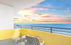 A balcony with a yellow wall, a glass table, and two wicker chairs.
