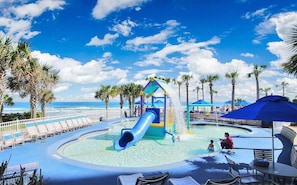 A water park with a blue slide, lounge chairs, and palm trees.