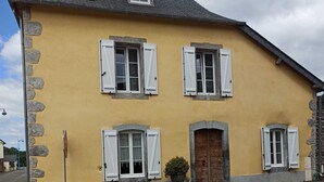A yellow building with white shutters, a wooden door, and a stone wall. - Gite Pouquette (Aramits)
