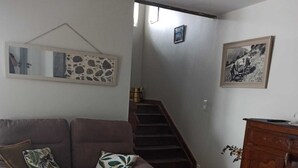 A living room with a brown sofa, a coffee table with decorative items, a wooden cabinet, and a staircase leading to another room. - Gite Pouquette (Aramits)