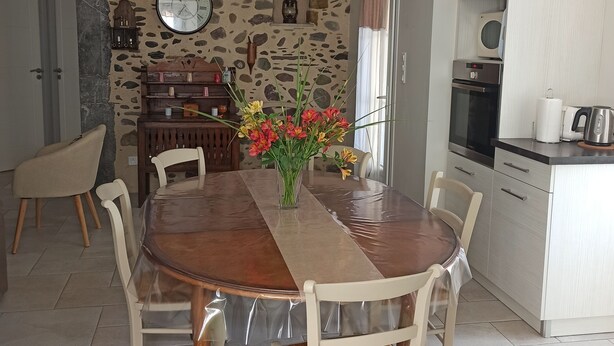 A dining area with a stone wall, a wooden table, and chairs. - Gite Pouquette (Aramits)
