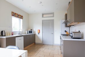 A kitchen with a dishwasher, microwave, toaster, and a window with a curtain.