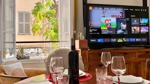 Ruokailutila, jossa on kahdelle katettu pöytä, viinipullo ja televisio, jossa näkyy kanavalista.