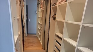 A narrow hallway with wooden flooring leading to a room with white shelving units.