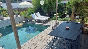 A wooden deck with a pool, lounge chairs, and a table with chairs.