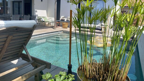 A pool area with a wooden deck, lounge chairs, and a small garden with tall plants.