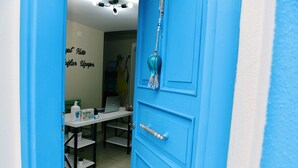 A blue door with a decorative tassel, a white table with a laptop and a bottle, and a wall with a mural. - Valitsa Otel (Bozcaada)