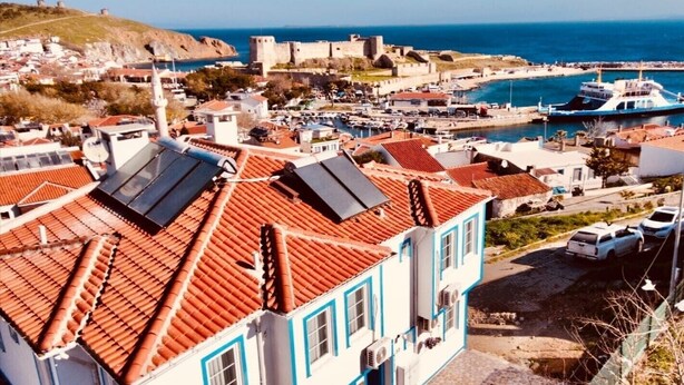 A coastal town with a prominent castle, terracotta-roofed buildings, and a marina with boats. - Valitsa Otel (Bozcaada)