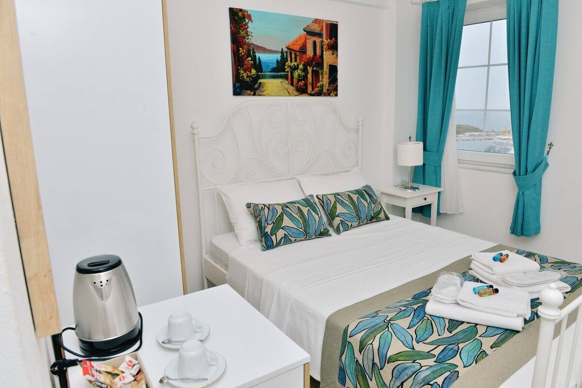 Une chambre d’hôtel avec un lit, une table de chevet avec une lampe, un tableau au mur et une fenêtre avec des rideaux.