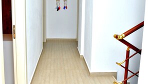 A hallway with a wooden door on the left, a dreamcatcher on the wall, and a wooden staircase on the right. - Valitsa Otel (Bozcaada)