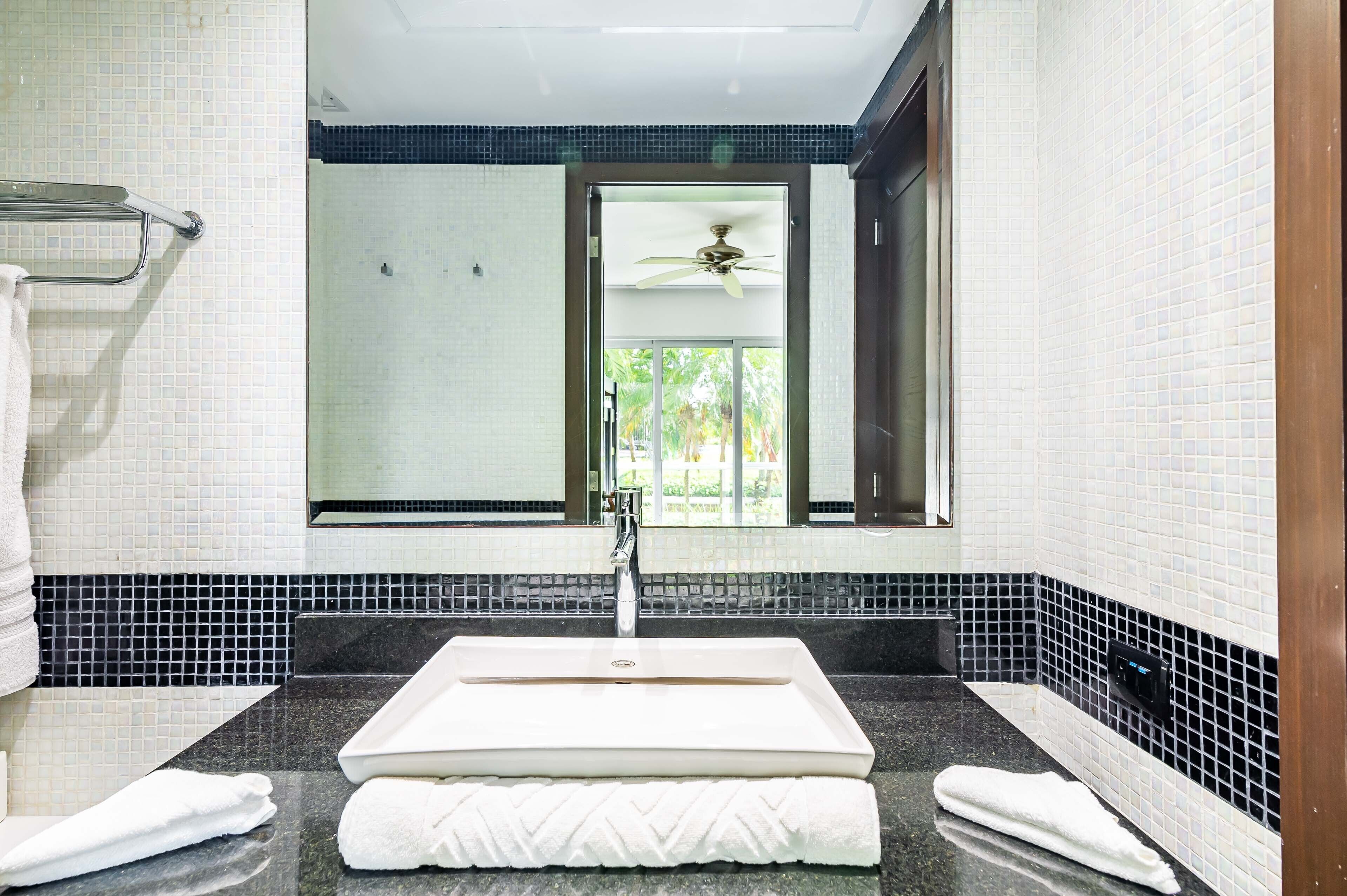 Un baño con lavamanos blanco, encimera negra y paredes de azulejos.