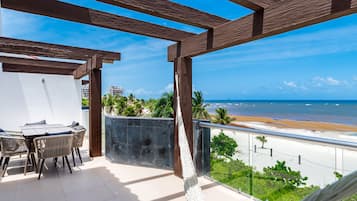 Un balcón con vista a la playa, una mesa con sillas y una hamaca.