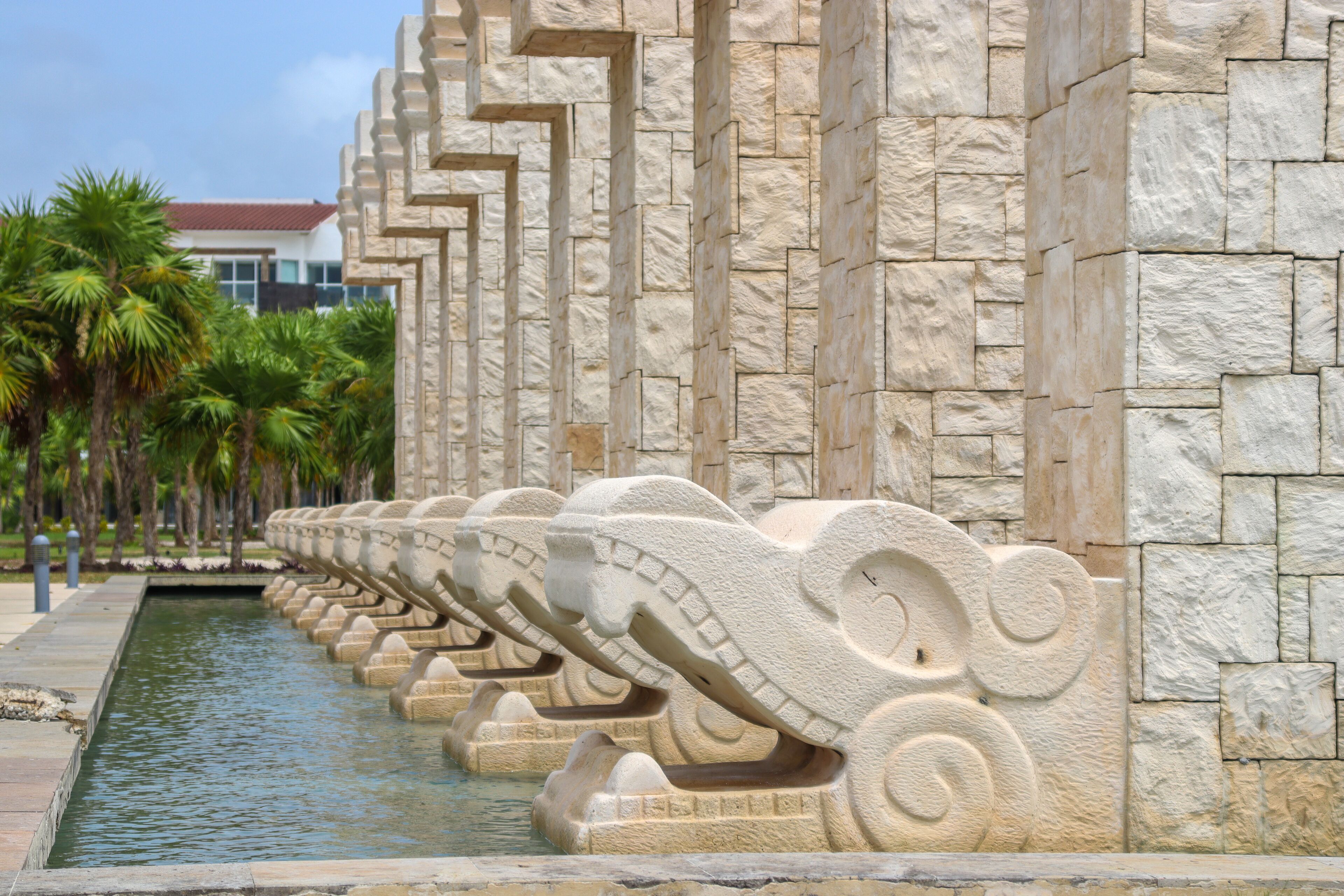 A stone wall with a series of carved animal heads along a water feature.