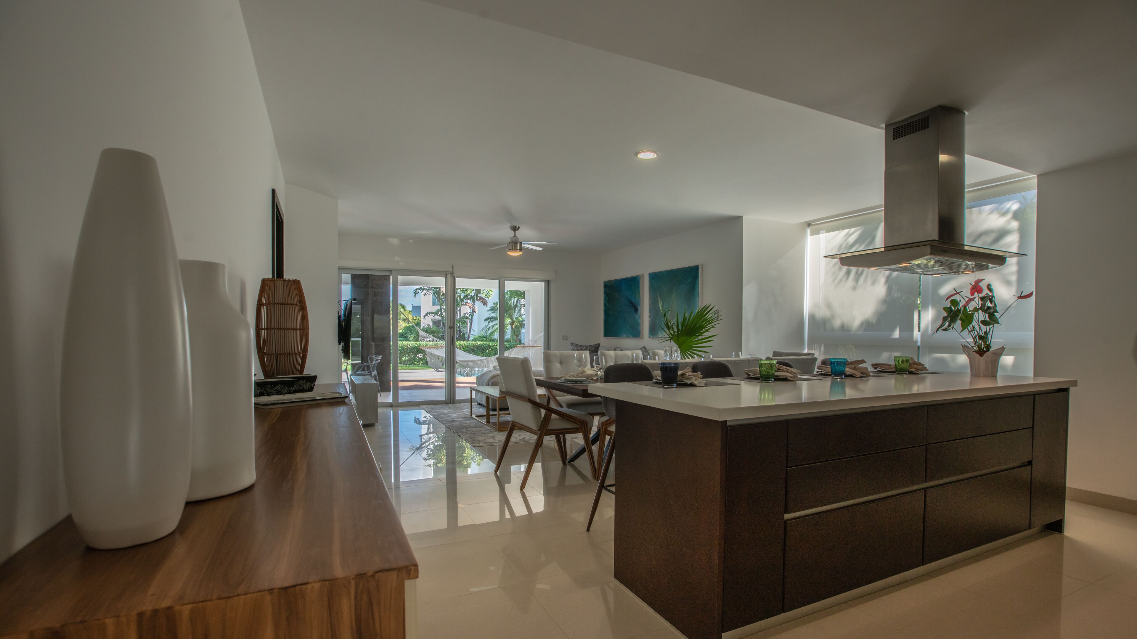 A modern kitchen with a central island, a dining area with chairs, and a view of the outdoors.
