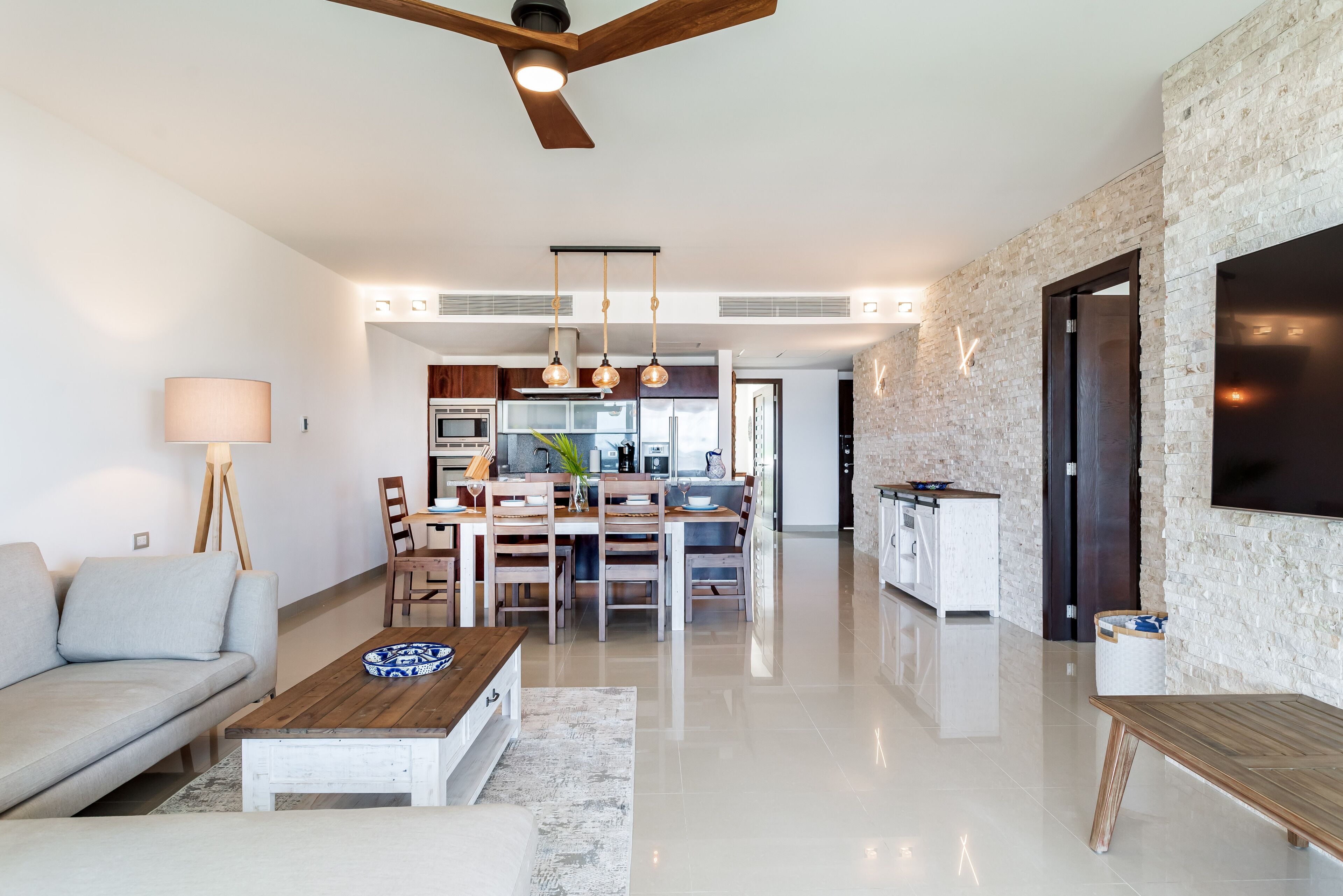 Een moderne woonkamer met een bank, salontafel en een eethoek. In de achtergrond is een keuken zichtbaar met een eettafel en stoelen.