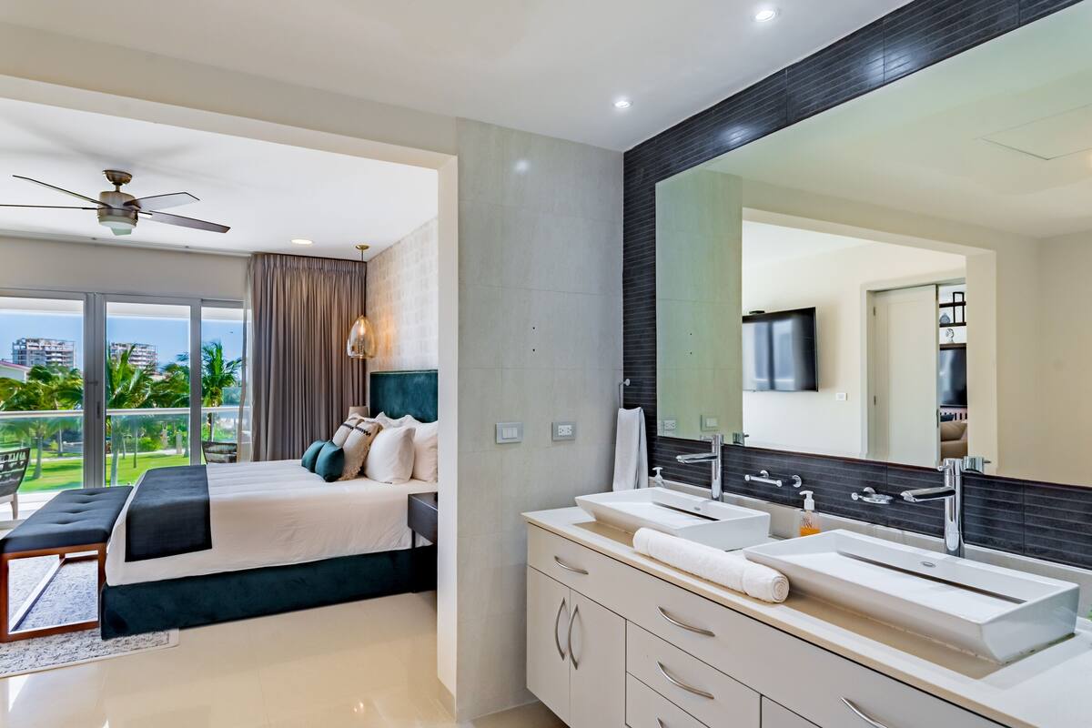 A modern bedroom with a large bed, a ceiling fan, and a balcony with a view of palm trees.