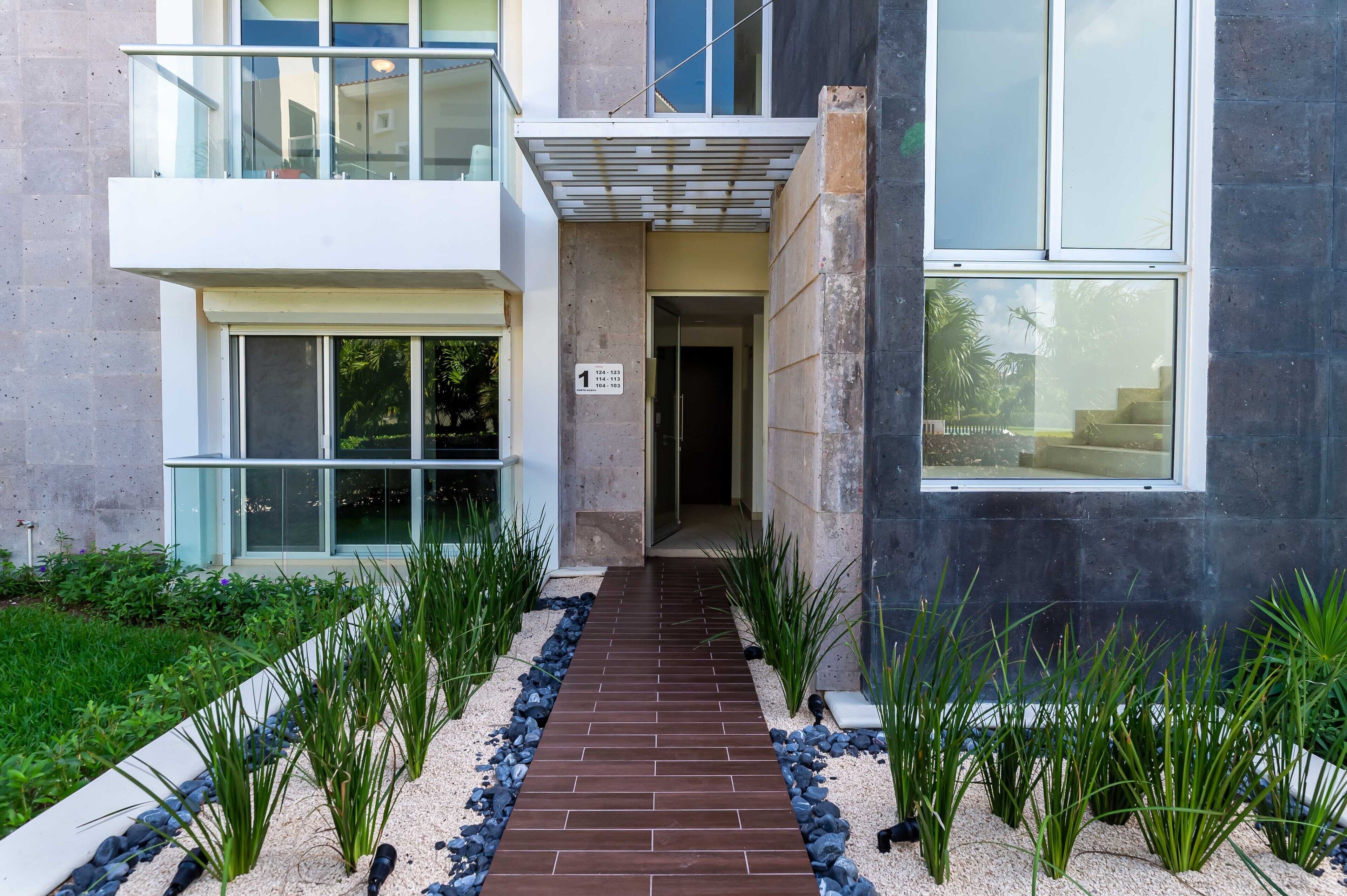 A modern building with a glass entrance, a brick pathway, and a sign indicating unit numbers.