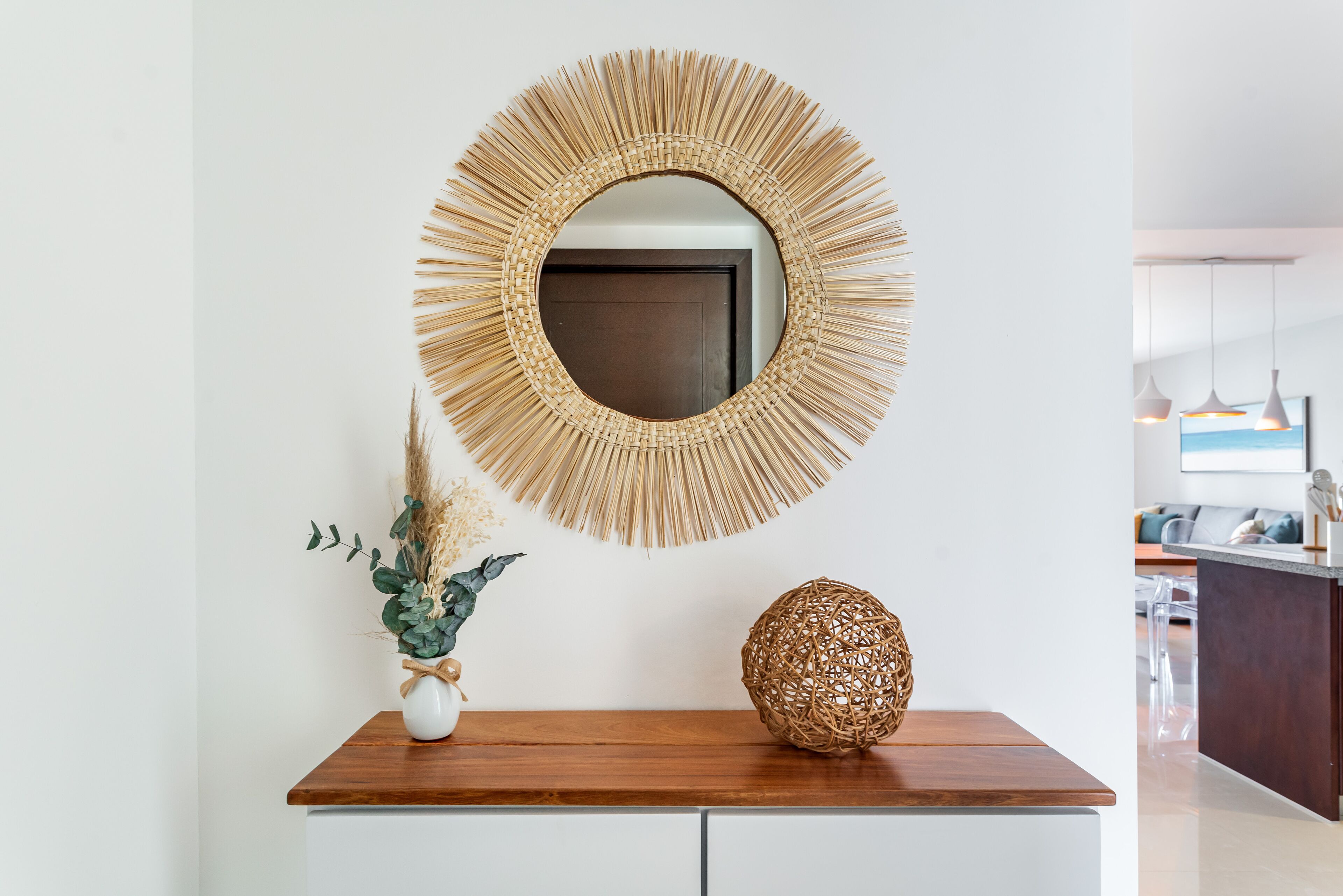 A modern interior with a round mirror on a wooden console, a vase with dried plants, and a textured spherical object.