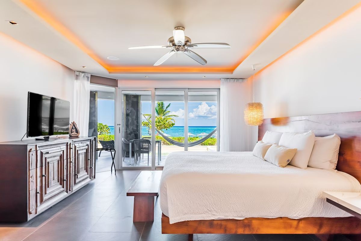 A hotel room with a bed, a TV, a desk, and a view of the ocean.