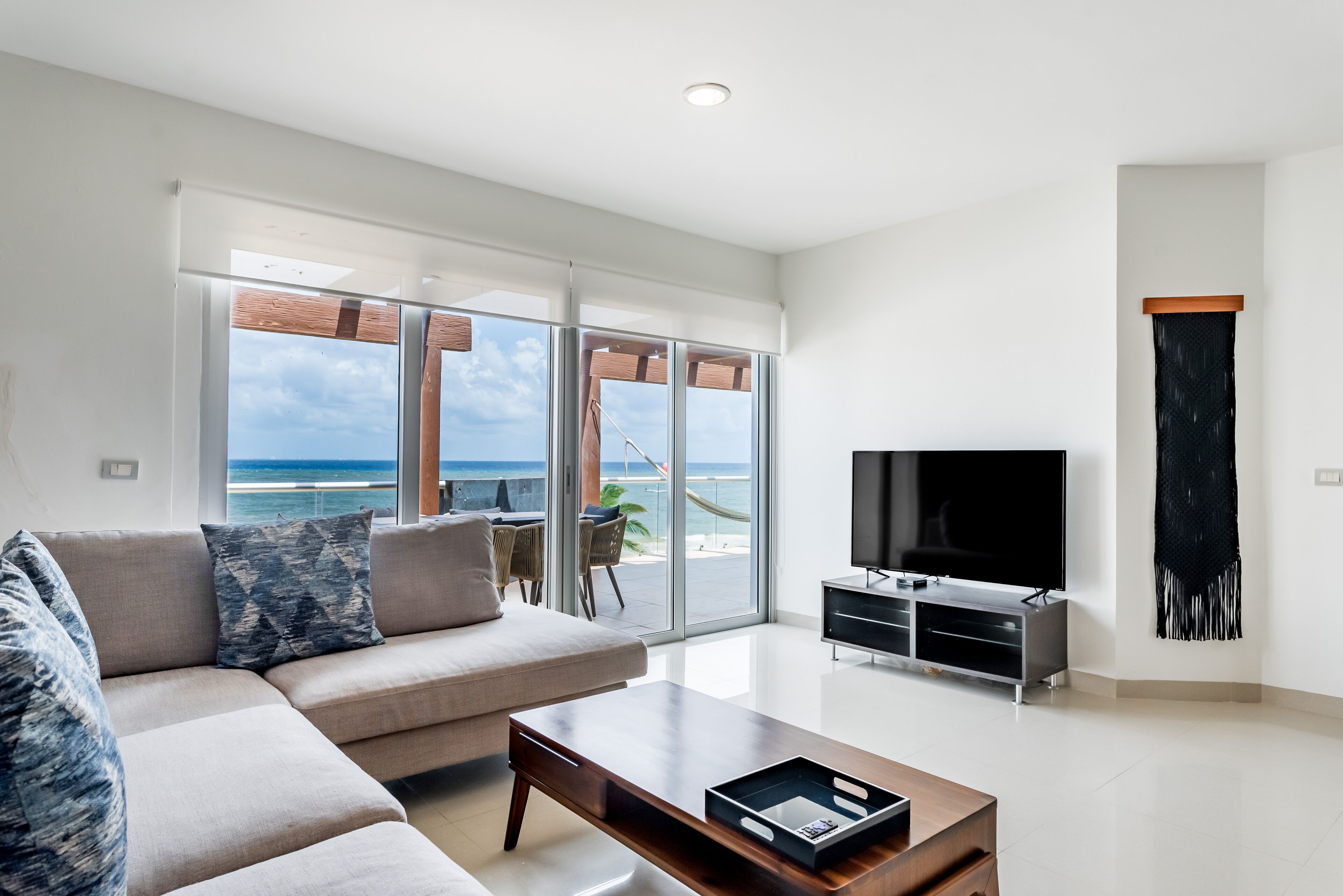 A modern living room with a sofa, coffee table, TV, and a balcony with a view of the ocean.
