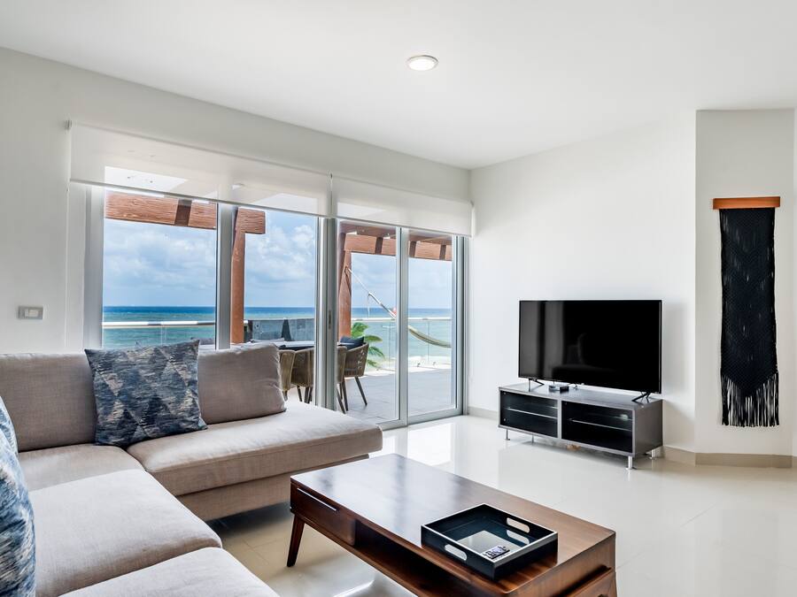 A modern living room with a sofa, coffee table, TV, and a balcony with a view of the ocean.