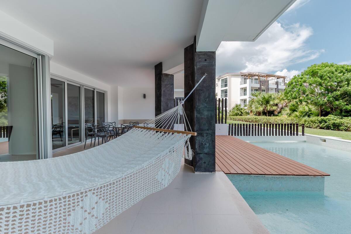 A hammock on a balcony with a pool, modern architecture, and a view of a residential building.