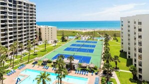 Un resort con múltiples canchas de tenis, piscina y vista al mar.