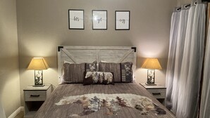 A bedroom with a bed, two bedside tables with lamps, a headboard, and three framed wall art pieces.