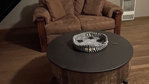 A room with a brown sofa, a round wooden table with a woven basket, and a staircase with a black railing.