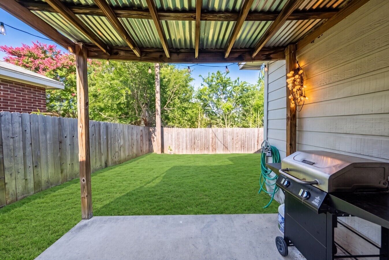 A backyard with a grill, a wooden fence, and a pergola structure.